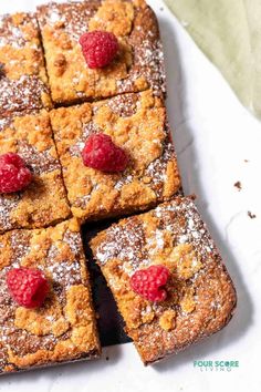 a white plate topped with square cakes covered in powdered sugar and raspberries