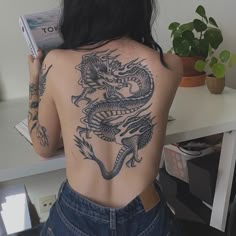 the back of a woman's body with tattoos on it, holding a book