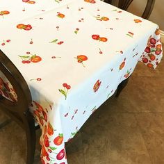 a dining room table covered with a white and red flowered tablecloth next to two chairs