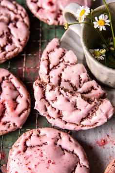 cookies with pink icing and flowers on a cooling rack next to a cup of tea