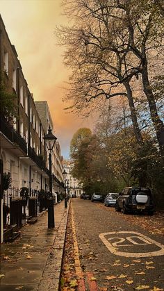 an empty street with parked cars on the side and trees lining the sidewalk in front