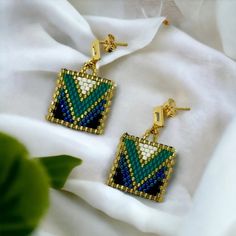 a pair of earrings sitting on top of a white cloth next to a green plant