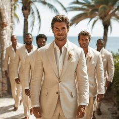 a group of men in white suits walking down a street next to palm trees and the ocean