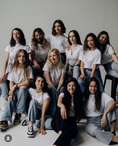 a group of women sitting next to each other in front of a white wall and floor