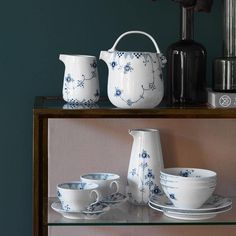 blue and white dishes are sitting on a shelf next to a coffee pot, teacup, and saucer