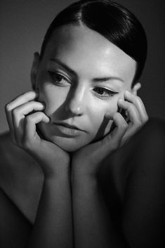 a black and white photo of a woman with her hands on her face looking at the camera