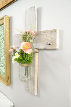 a cross hanging on the wall with flowers in a mason jar and an old wooden frame