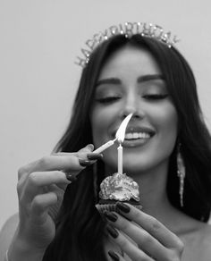 a woman wearing a tiara holding a lit candle in front of her face and smiling