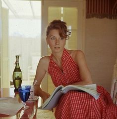 a woman sitting at a table with a book in her hand and two glasses on the table