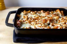 a casserole dish with meat and cheese in it sitting on a table next to a blue towel