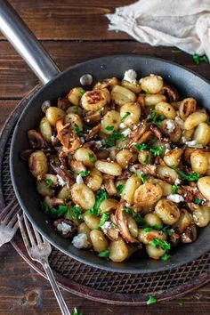 a pan filled with potatoes and mushrooms covered in parmesan cheese on top of a wooden table