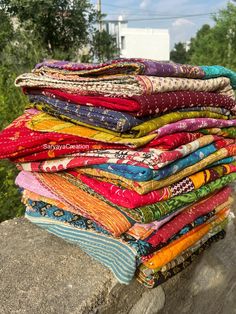 a stack of colorful fabrics sitting on top of a stone wall