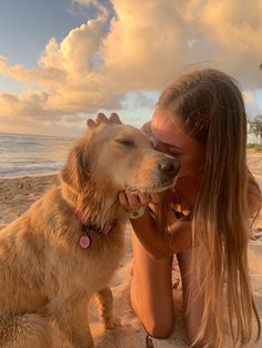 a woman sitting on the beach with her dog next to her and kissing her nose