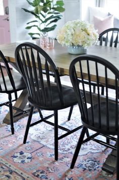 a dining room table with black chairs and flowers