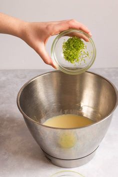 someone is adding some green stuff to their food in a metal bowl on the counter