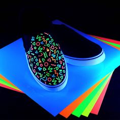 a pair of shoes is lit up with neon colors on the floor next to colored papers