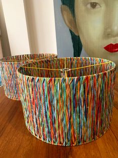 two colorful baskets sitting on top of a hard wood floor next to a painting with a woman's face