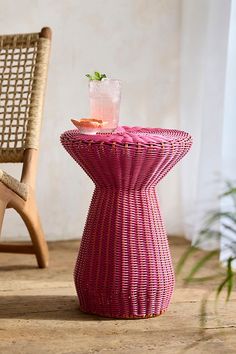 a wicker table with a drink on it next to a chair and potted plant