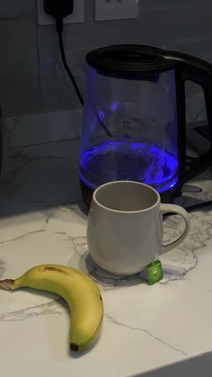 a banana sitting on top of a counter next to a coffee pot and a cup