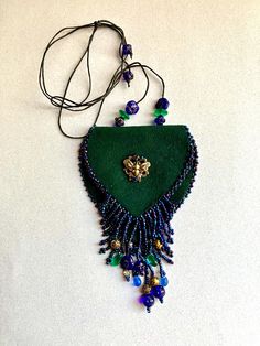 a green purse with beads hanging from it's side on a white table next to a black cord