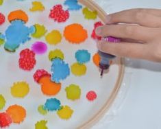 a person is drawing on a plate with colored dots and crayon pens in front of them