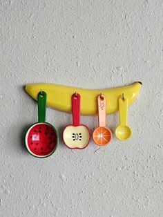 an assortment of kitchen utensils hanging on a wall with a banana and watermelon