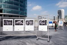 an open area with posters and people walking around it in front of a tall building