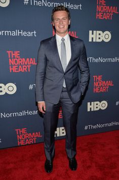 a man in a suit and tie standing on a red carpet at the normal heart