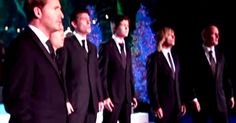 a group of men standing next to each other in front of a blue christmas tree