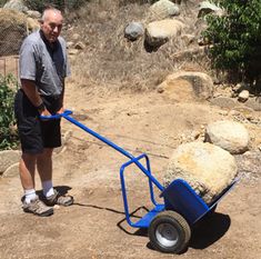 a man standing next to a blue wheelbarrow on top of a dirt field