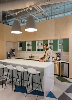 a man standing at the counter in a kitchen next to four bar stools and an oven