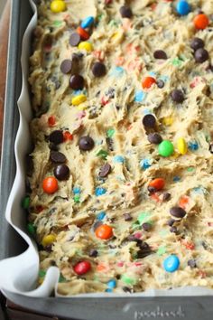 an uncooked cookie dough with m & m and chocolate chips on top in a pan