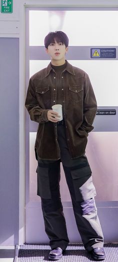 a young man standing in front of a wall holding a coffee cup and looking at the camera