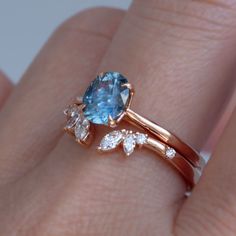 a close up of a person's hand holding a ring with an aqua and white diamond