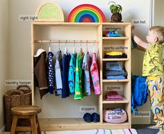 a little boy standing in front of a wooden shelf with clothes on it and a rainbow rug