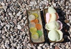 two trays filled with different colored candies sitting on top of gravel covered ground