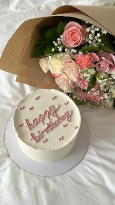 a birthday cake and bouquet of flowers on a bed