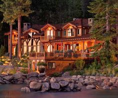 a large house sitting on top of a lake next to a lush green forest covered hillside