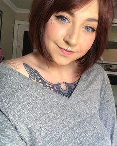 a woman with piercings on her neck is smiling at the camera while wearing a grey shirt