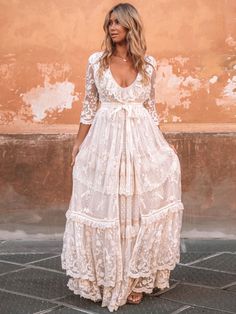 a woman standing in front of a wall wearing a white dress with long sleeves and an open back