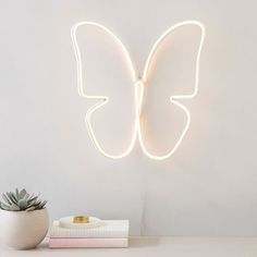 a white butterfly shaped neon light on a wall next to a potted succulent