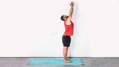 a man standing on a blue mat in front of a white wall with his arms up