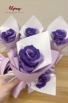 purple flowers are wrapped in white paper and being held by someone's hand