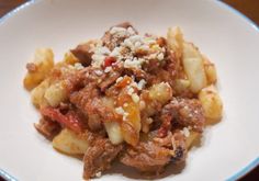 a white plate topped with pasta and meat covered in sauce on top of a wooden table