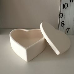 a white heart shaped box sitting on top of a table next to a clock face