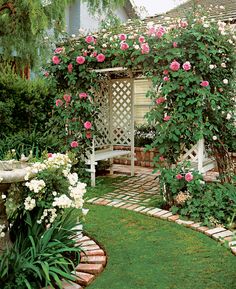 a garden with roses growing on the side of it and a bench in the middle