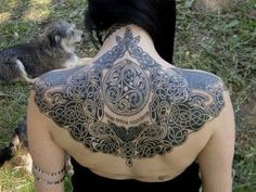 the back of a man's body with tattoos on it and a dog standing next to him