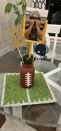 a football themed centerpiece on top of a glass table with grass and fake plants