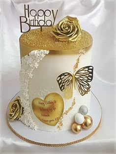 a white and gold birthday cake with butterflies on it's top, surrounded by other decorations