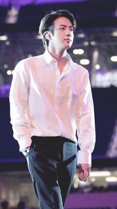 a male in a white shirt and black pants is standing on stage with his hands in his pockets